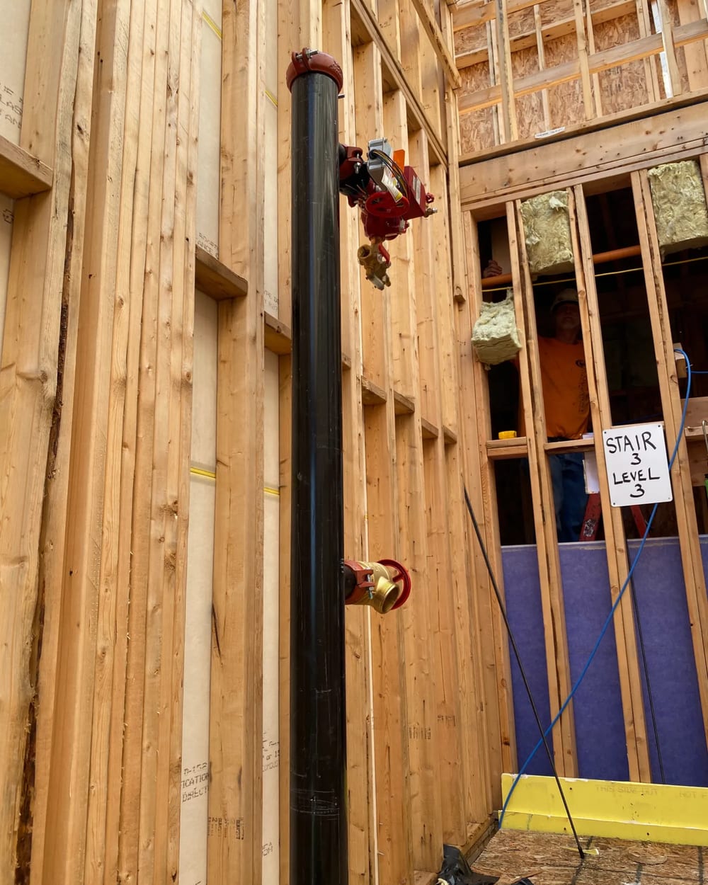 Standpipe riser with a hose valve and control valve in a wood-frame stair shaft at Stair 3, Level 3
